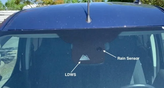 Top of a windshield from outside: a triangle-shaped lane departure warning (LDWS) camera window and a small round rain sensor next to it