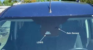 A triangle-shaped lane departure camera window and a small round rain sensor at the top of a windshield