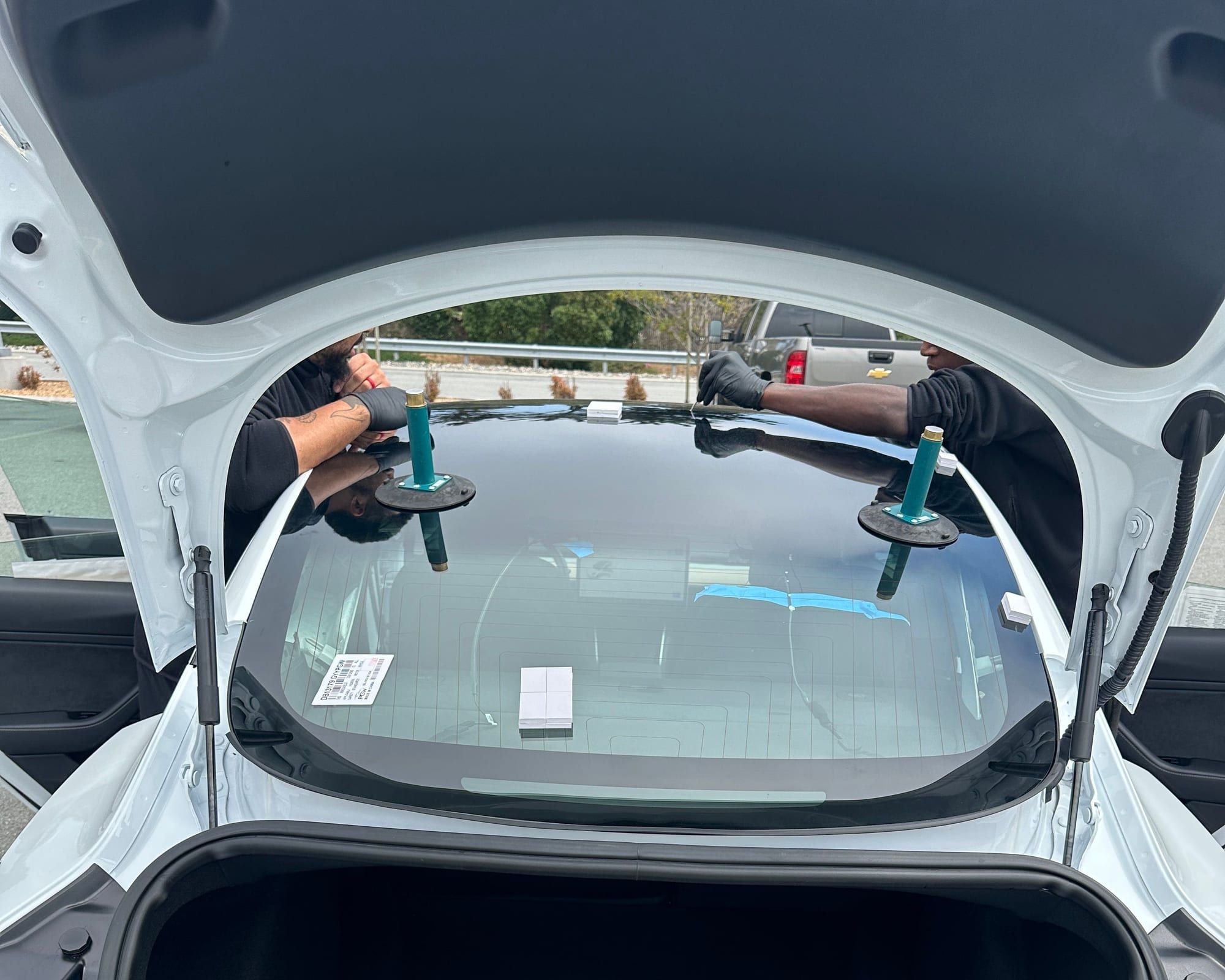 Two Super Auto Glass technicians setting new glass on a white Tesla Model 3
